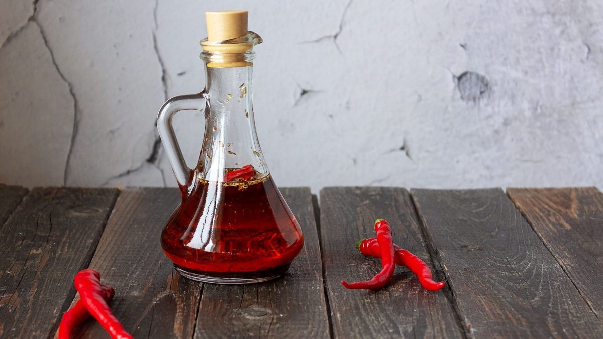 In einer durchsichtigen Karaffe aus Glas ist selbstgemachtes Chili-Öl. Drum herum liegen rote Chili-Schoten.