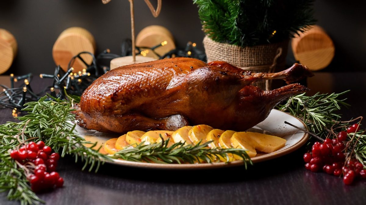 Eine knusprig gebackene Ente auf einem weißen teller und drum herum weihnachtliche Dekoration.