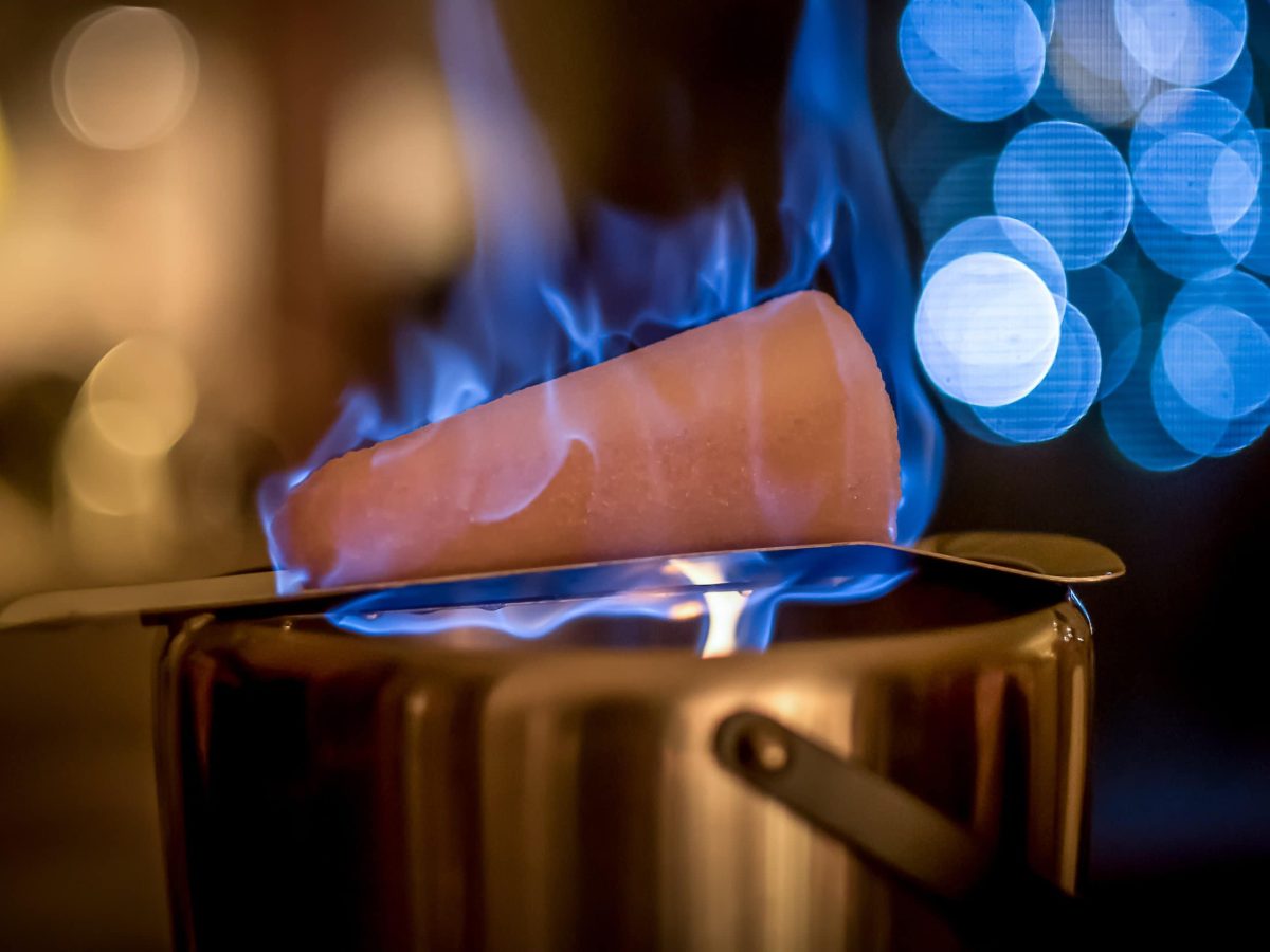 Ein Topf mit Feuerzangenbowle, auf dem ein brennender Zuckerhut liegt.