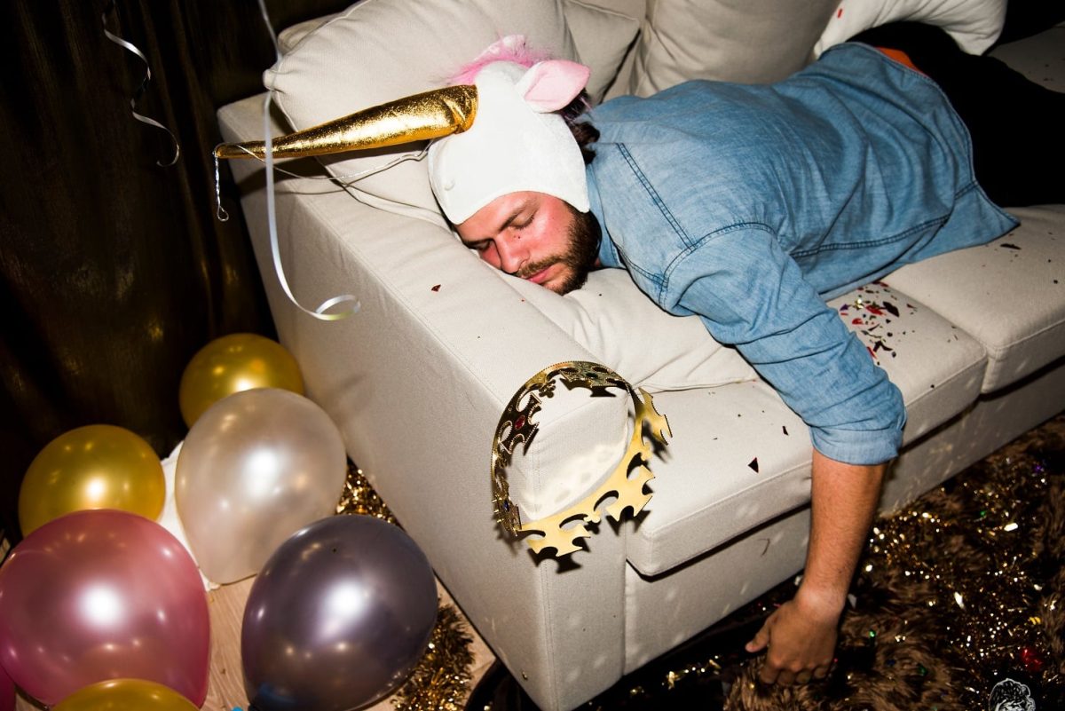 Ein schlaftrunkener Mann liegt nach einer Party bäuchlings auf der Couch.