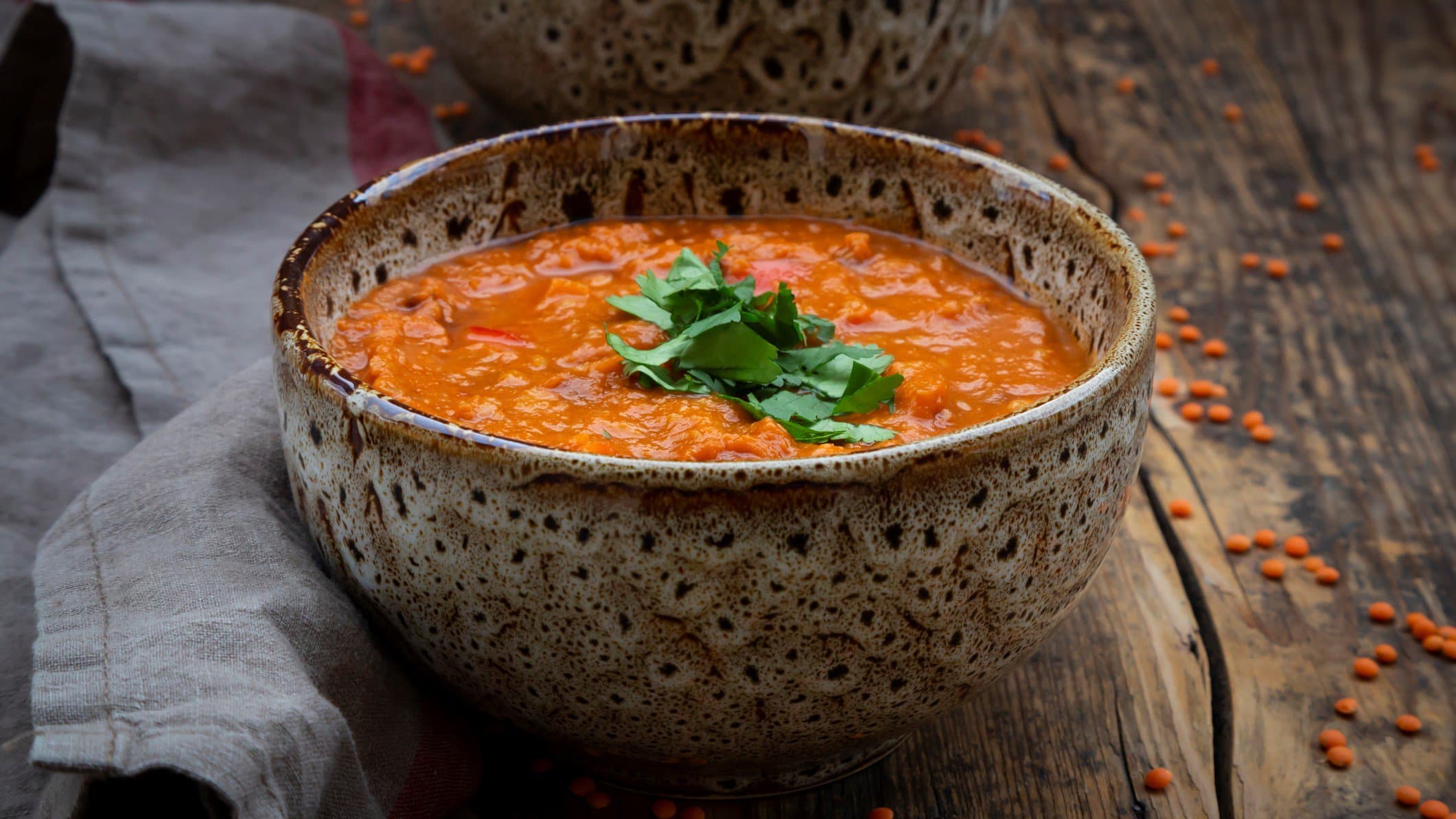 Eine Schüssel Ofengemüse-Suppe bestreut mit frischer Petersilie oder Koriander auf einem Holztisch, daneben ein Geschirrtuch.