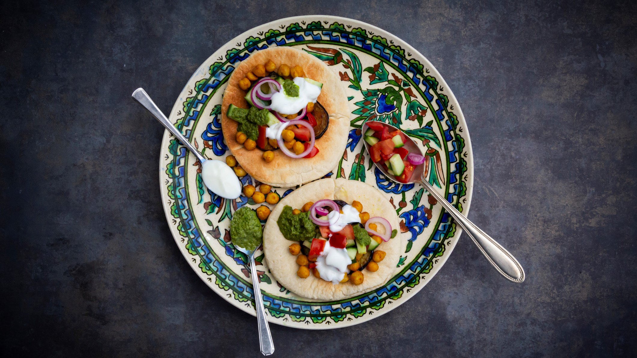 Ein arabisch bemalter Teller mit Sabich, Pitafladen belegt mit Gemüse und einer weißen sowie grünen Soße.