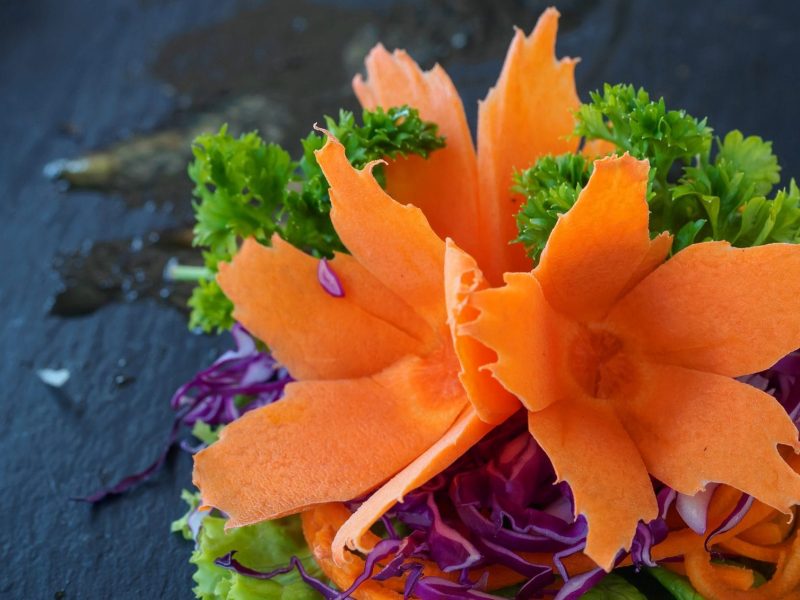 Eine Möhre wurde tourniert. Also on Form einer Blüte geschnitten. Sie dekoriert ein Salatblatt.