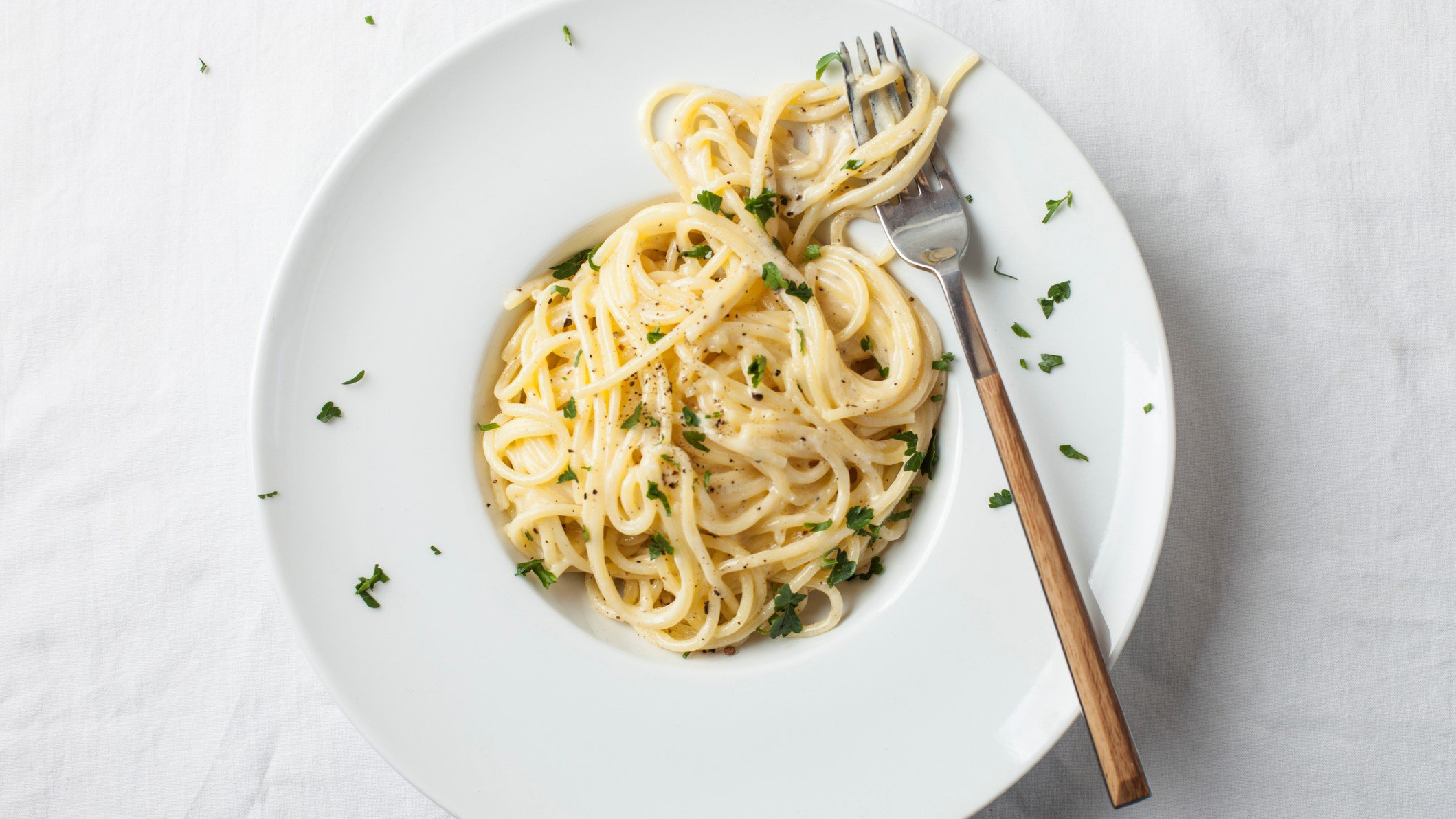 Ein Teller mit veganen Spaghetti Alfredo in der Draufsicht, darauf liegt eine Gabel.