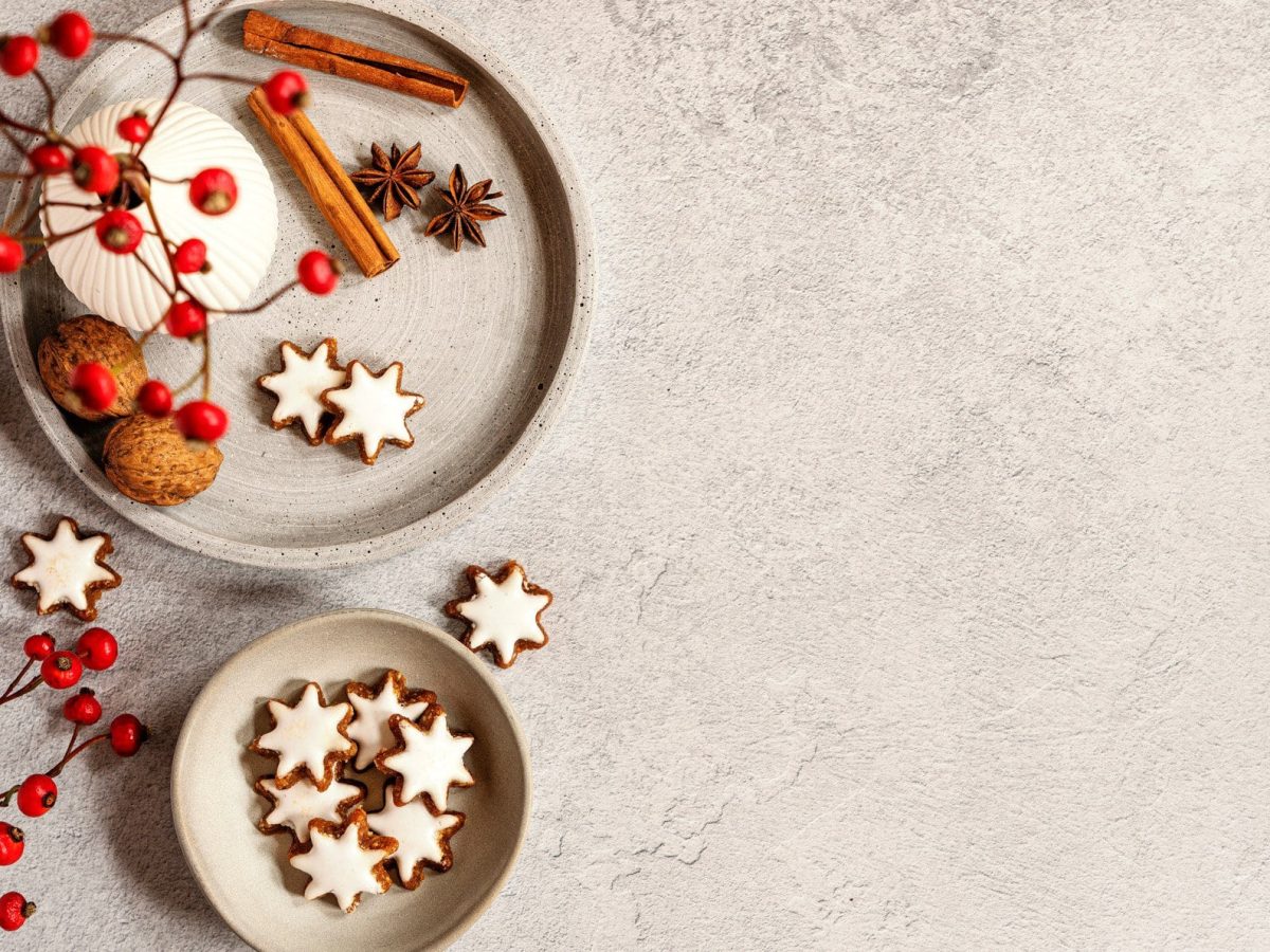 Ein Teller und eine Schale mit veganen Zimtsternen in der Draufsicht auf hellem Untergrund, außerdem Walnüsse, Anis und Zimtstangen sowie ein Weihnachtsstrauß.