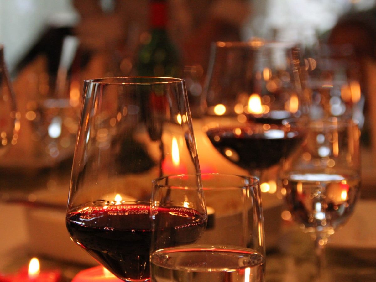 Passende Weine zum Weihnachtsmenü auswählen. Gläser mit Rotwein und Weißwein auf festlicher Tafel. Frontalansicht.