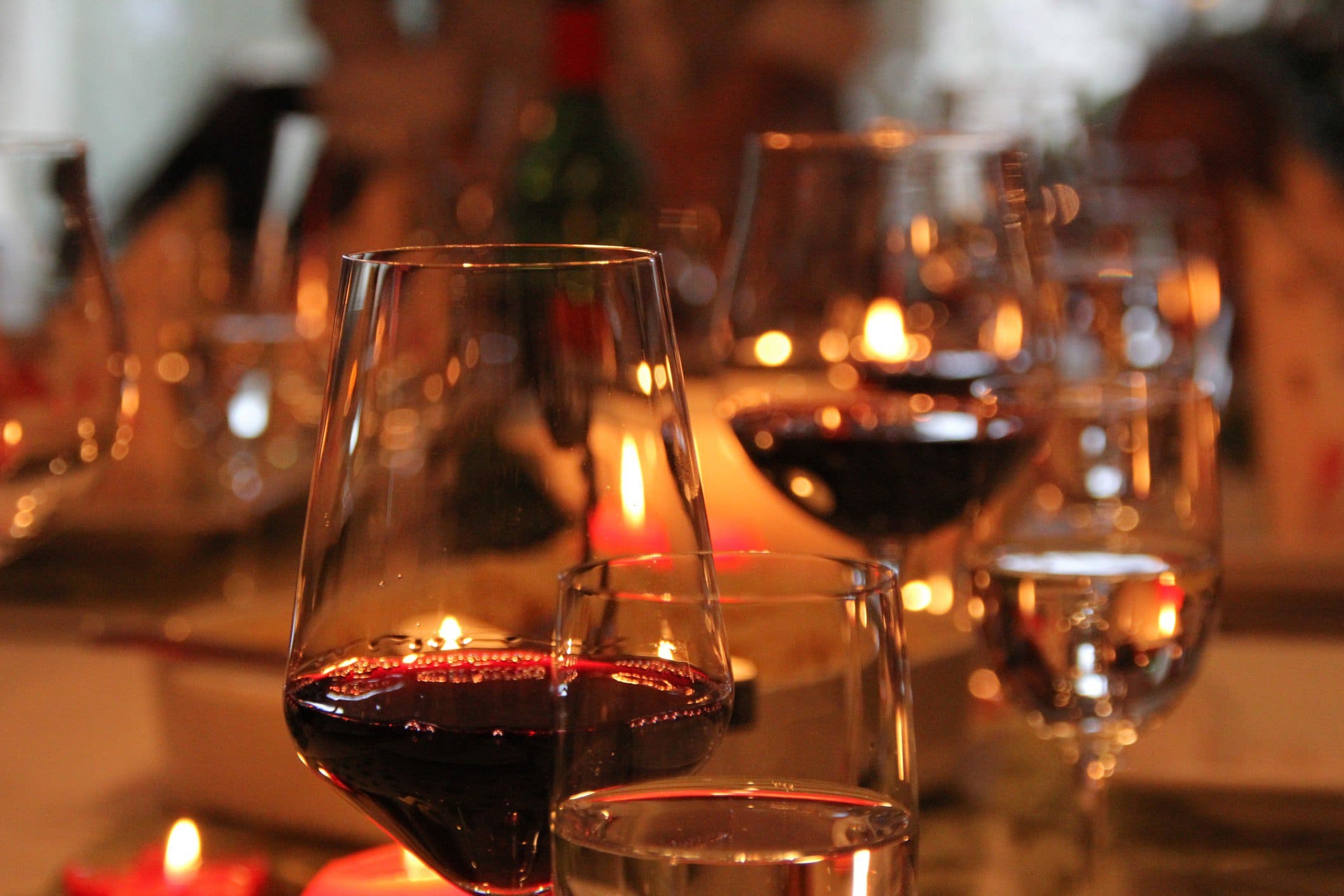 Passende Weine zum Weihnachtsmenü auswählen. Gläser mit Rotwein und Weißwein auf festlicher Tafel. Frontalansicht.