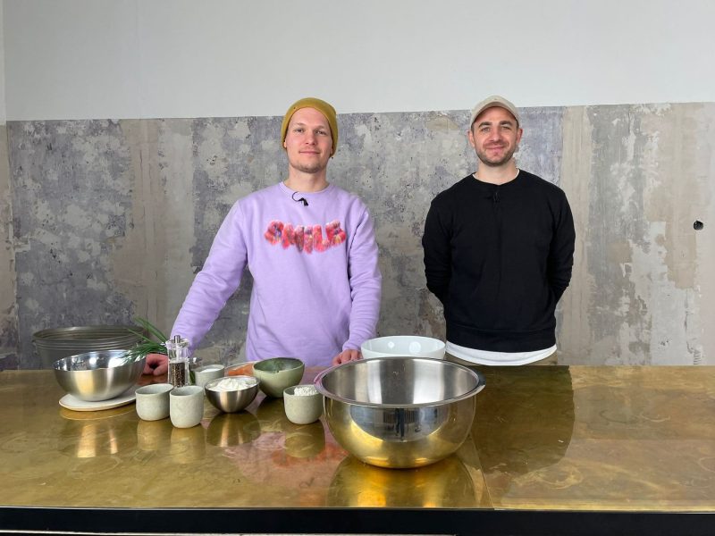 Food-Stylist Fabian Dietrich und EAT CLUB-Redakteur Robin Schmidt stehen hinter der Theke im Frevel, einem Weinhandel in Berlin-Neukölln. Vor ihnen stehen die Zutaten für einen Flammkuchen.
