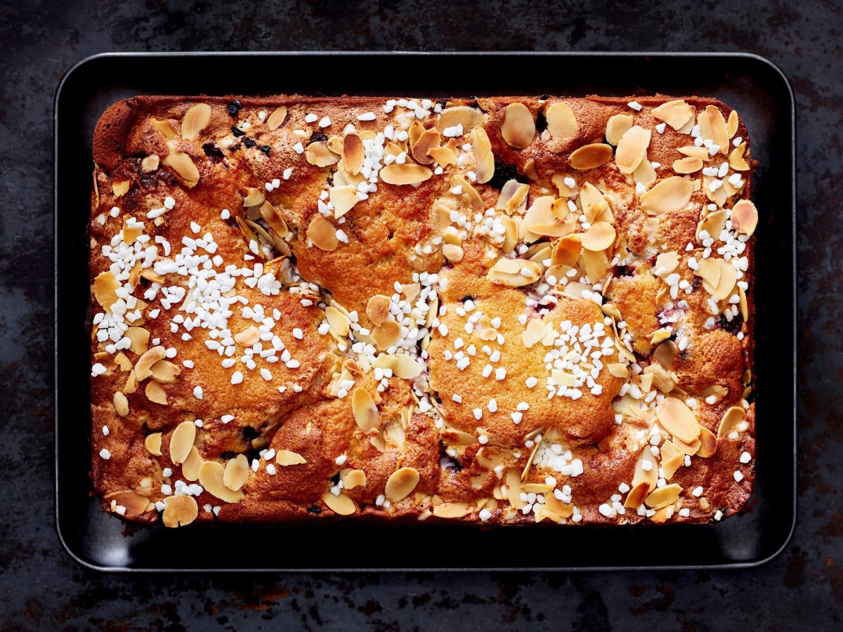 Auf einem Blech liegt ein Butter-Beeren-Kuchen. Er ist dekoriert mit Mandelraspeln und Zucker.