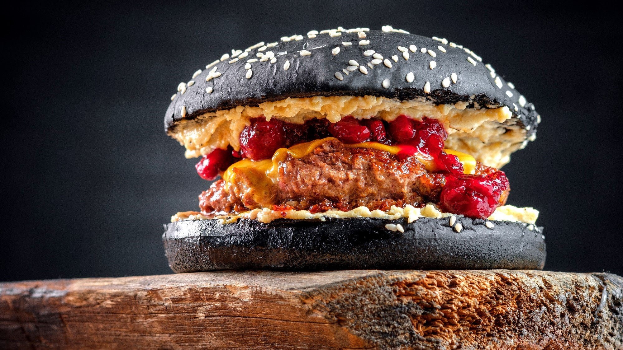 Ein Burger mit Cranberry-Sauce in schwarzen Burgerbuns steht auf einem dunklen Holzbrett vor einem schwarzen Hintergrund