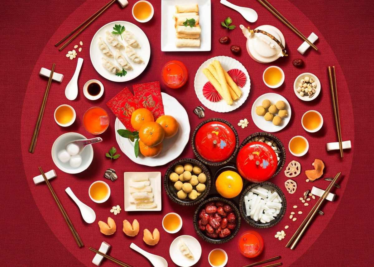Eine Auswahl an verschiedenen traditionellen Gerichten des chinesischen Neujahrsessen in einem Kreis angeordnet vor einem roten Hintergrund, von oben.