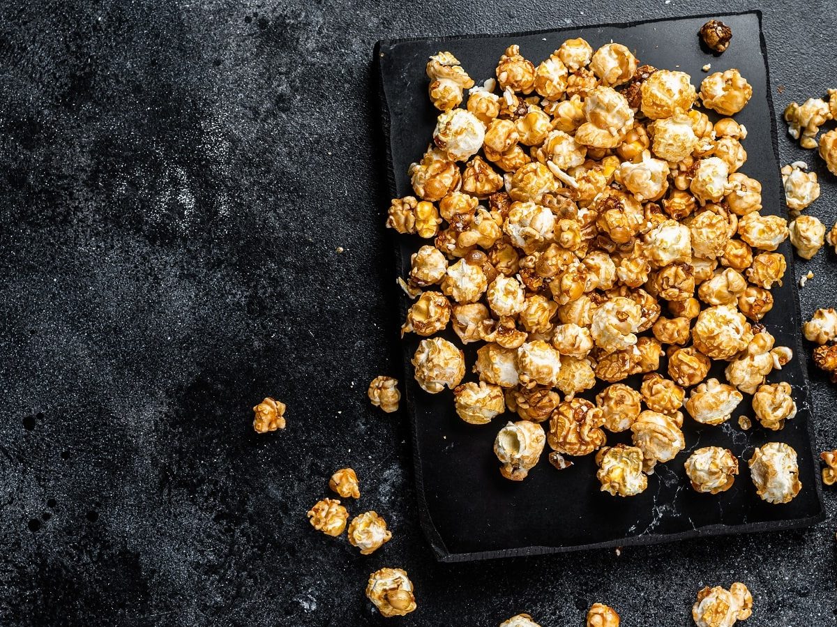 Knuspriges Karamell-Popcorn selbst gemacht im Ofen, auf einem schwarzen Backblech vor einem schwarzen Hintergrund, von oben.
