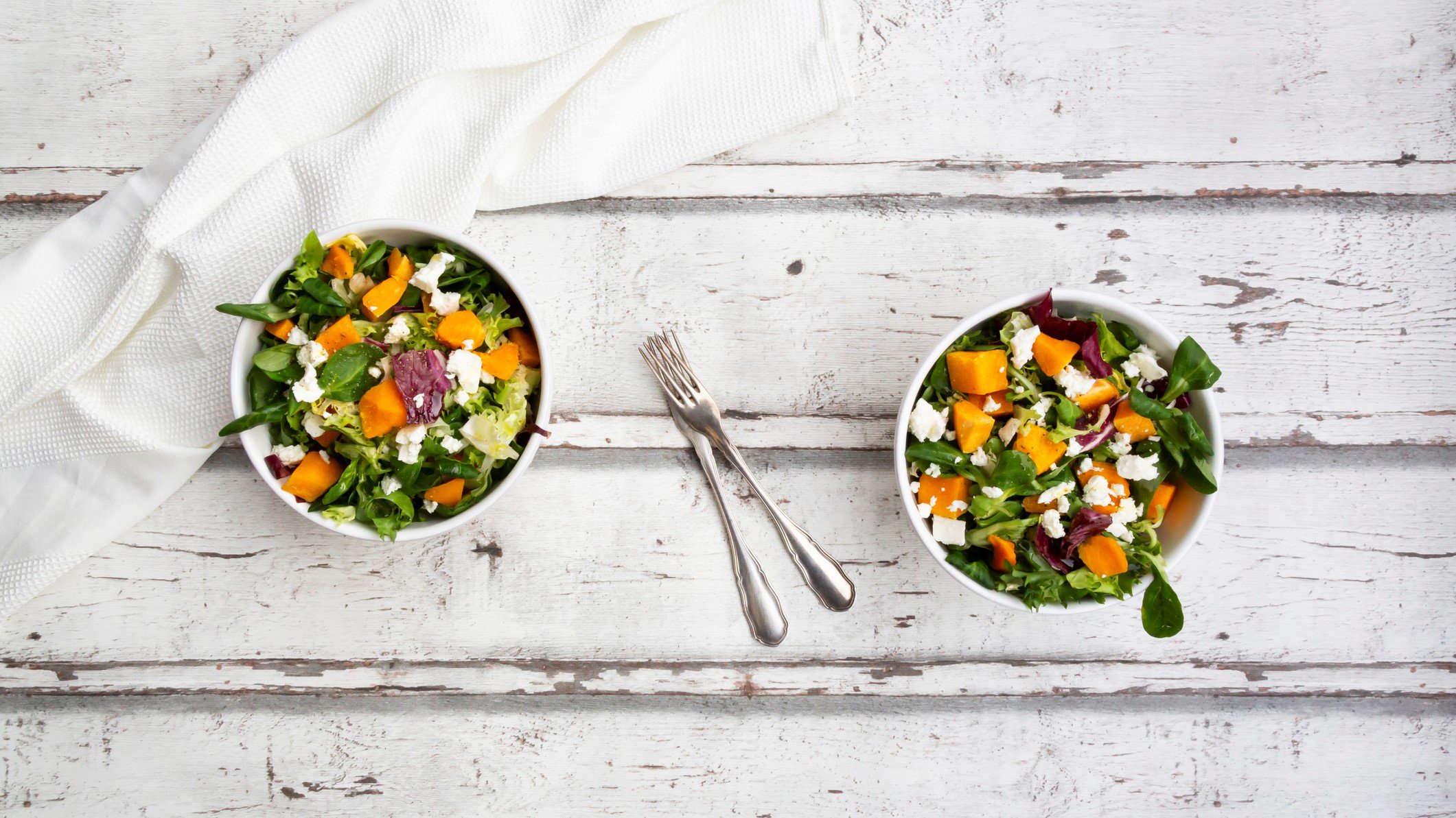 Zwei Schüsseln lauwarmer Salat mit Ofengemüse auf hellem Holz in der Draufsicht.