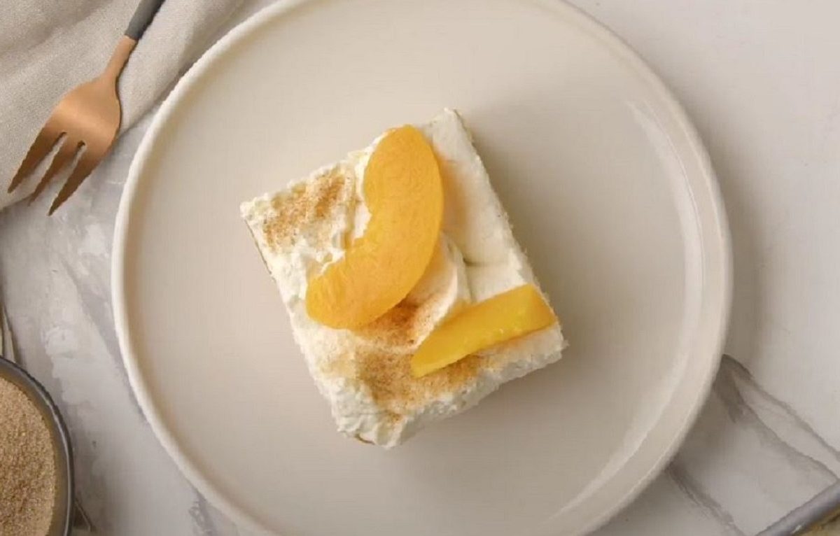 Ein Stück Pfirsich-Schmandkuchen platziert auf einem weißen Teller.