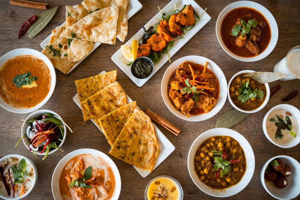 Verschieden indische Gericht mit Naan und Chicken Currys zum Tag des Chicken Currys auf einem Tisch angerichtet. Aufnahme aus der Vogelperspektive.