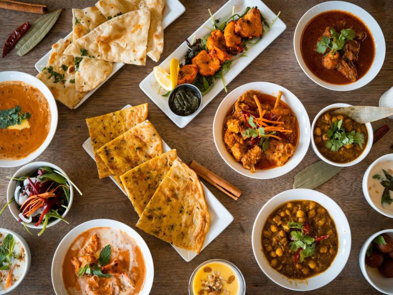 Verschieden indische Gericht mit Naan und Chicken Currys zum Tag des Chicken Currys auf einem Tisch angerichtet. Aufnahme aus der Vogelperspektive.