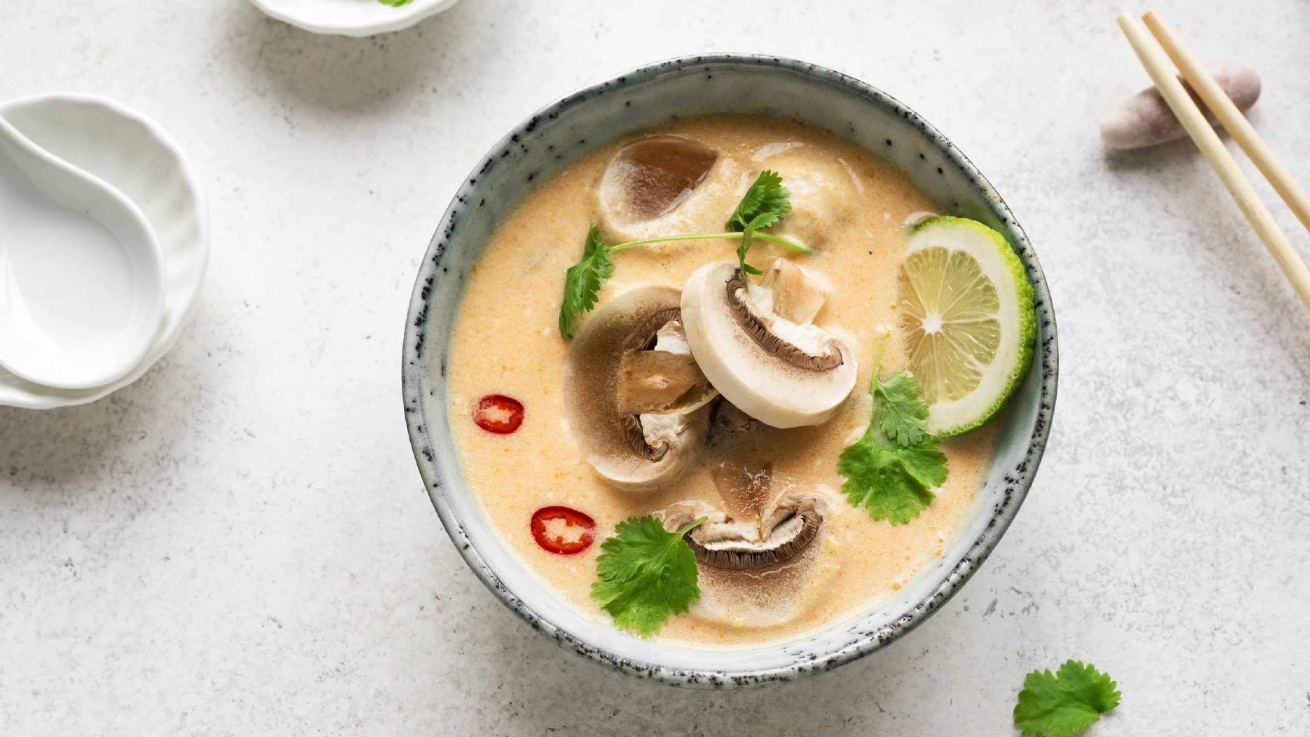 Tom Kha Hed, vegane thailändische Suppe mit Kokosmilch, Zitronengras, Ingwer, Pilzen, Chili, Limette und Chili in einer hellen Schale auf weißem Hintergrund
