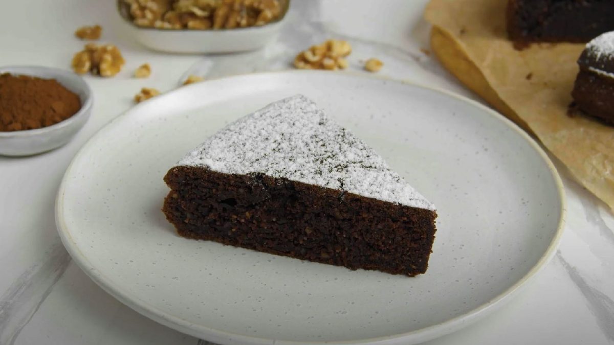 Ein Stück vom Walnuss-Schüttelkuchen mit Schokolade platziert auf einem weißen Teller.