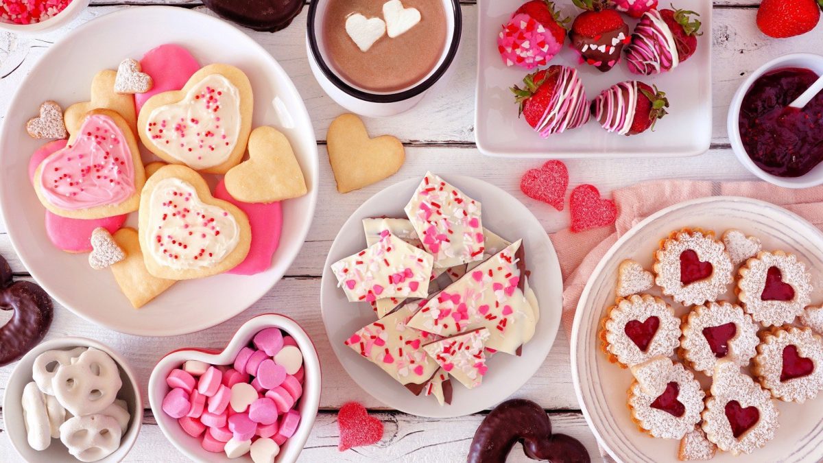 Auf einem weißen Tisch ist ein romantisches Büfett zum Valentinstag angerichtet. Auf dem Tisch stehen unterschiedliche süße Speisen.