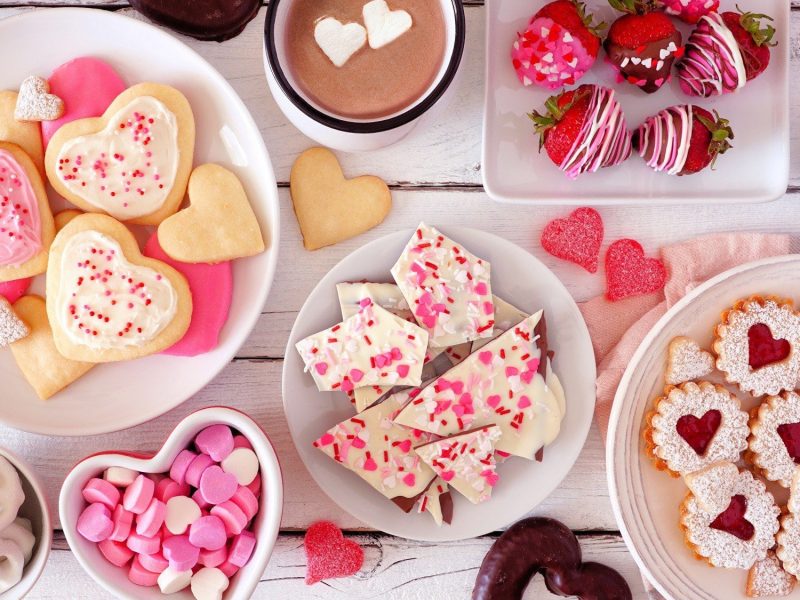 Auf einem weißen Tisch ist ein romantisches Büfett zum Valentinstag angerichtet. Auf dem Tisch stehen unterschiedliche süße Speisen.