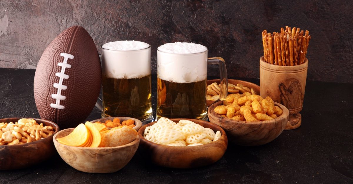 Zwei Bier, verschiedene Snacks und ein Football vor dunklem Hintergrund