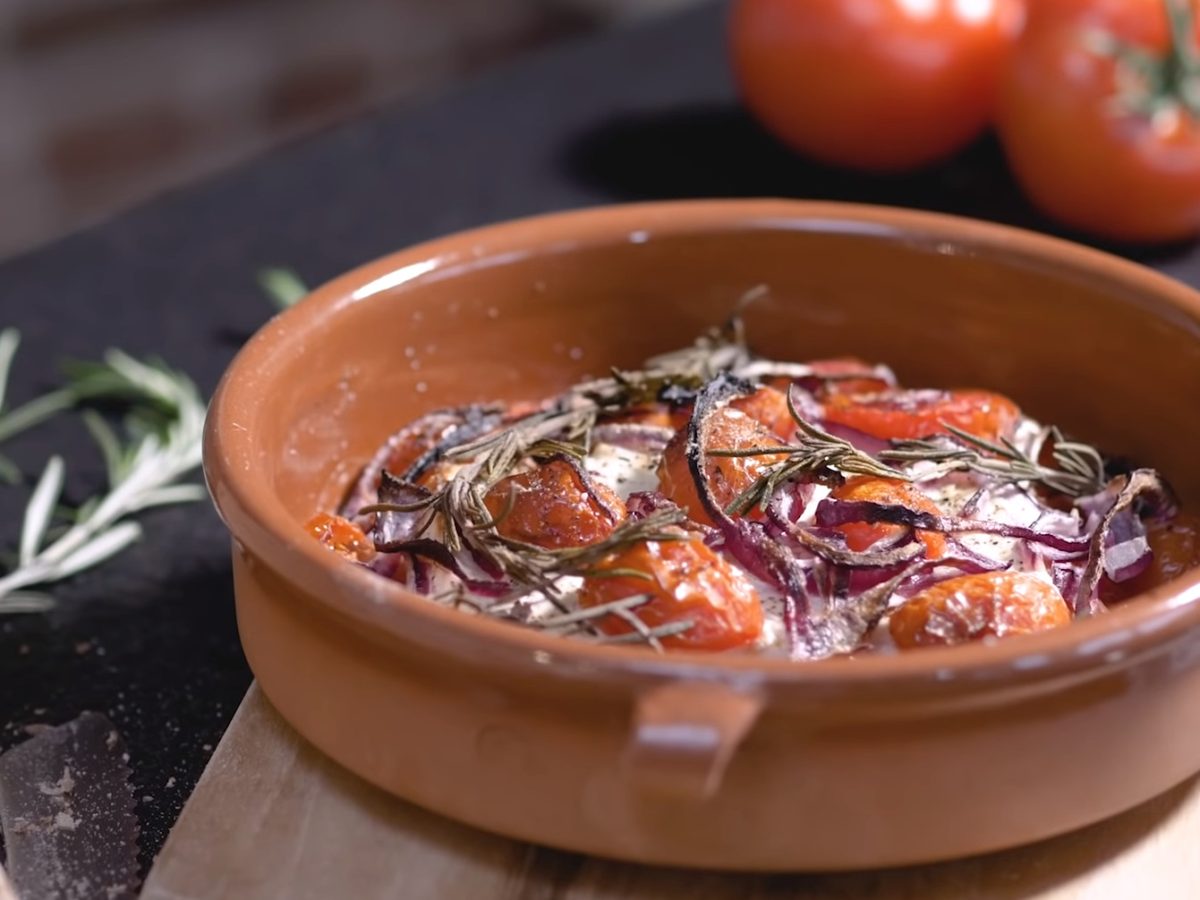 gebackener Feta mit Tomaten in Terracotta-Schale auf einem Holzbrett.
