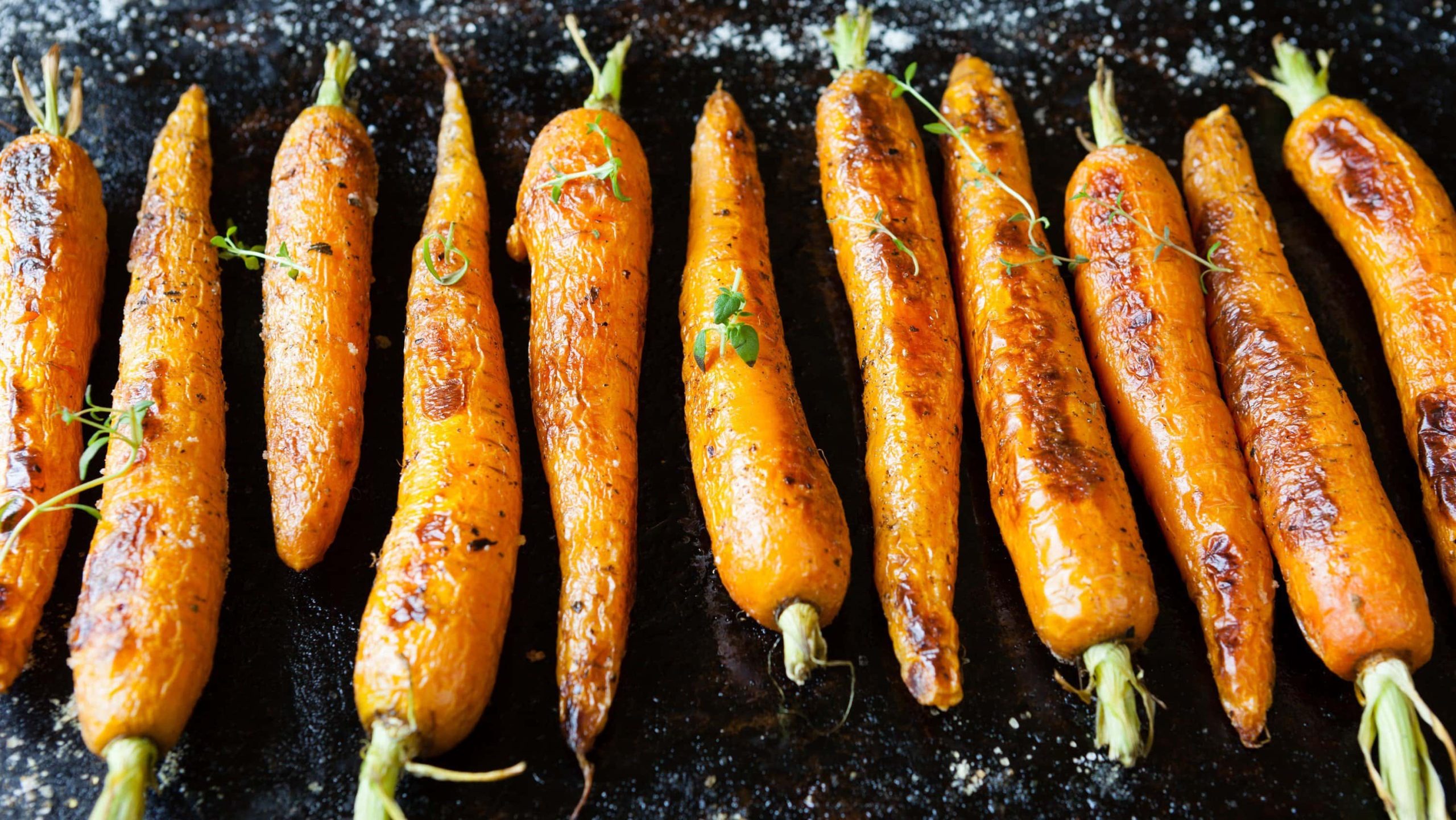 Im Ofen geröstete Karotten mit Ingwersauce auf einem Schieferbrett ausgebreitet und mit frischen Kräutern garniert