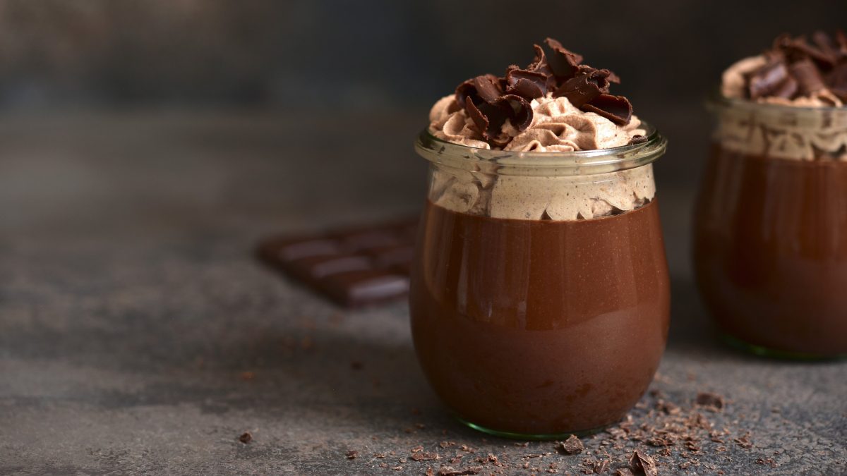 Guinness Schoko Pudding in einem Glas. Daneben Schokolade. Das ganze auf einem dunklen Untergrund.