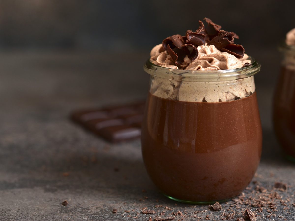Guinness Schoko Pudding in einem Glas. Daneben Schokolade. Das ganze auf einem dunklen Untergrund.