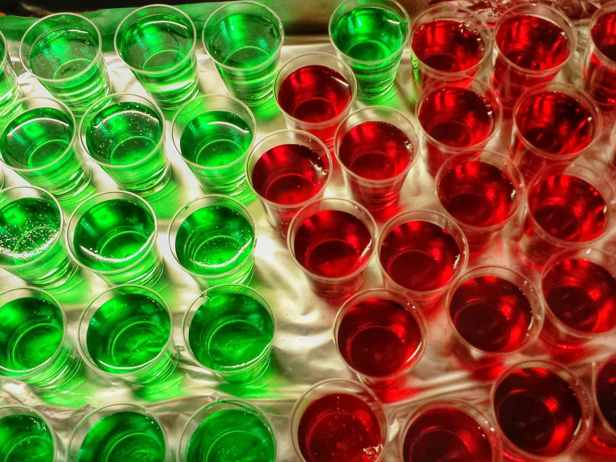 Grüne und rote Jell-o Shots Jelly Shots in kleinen Gläsern auf hellem UNtergrund. Aufnahme aus der Vogelperspektive.