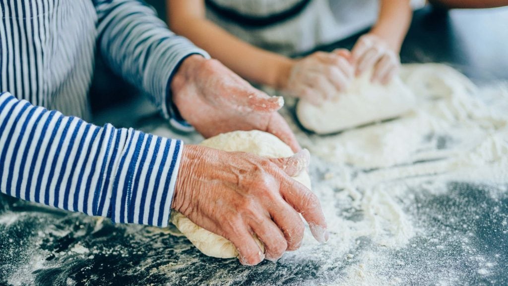 Großmutter und Kind kneten gemeinsam Lievito Madre Teig auf einer Platte mit viel Mehl