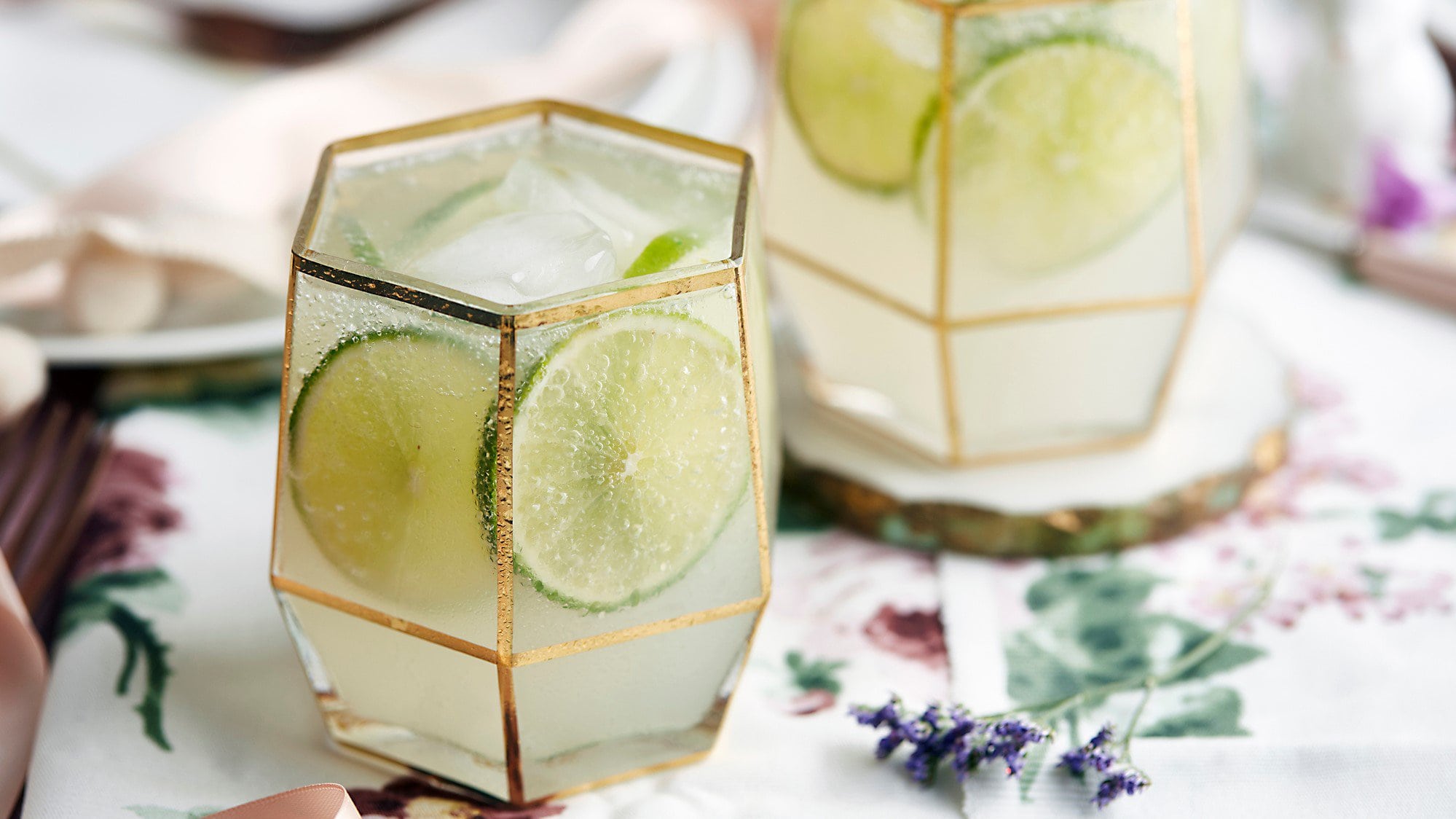 Zwei Gläser Limetten-Ingwer-Limo mit Limettenscheiben und Eiswürfeln.