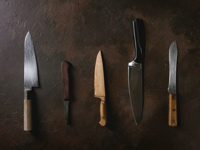 Vor einem dunklen Hintergrund liegen fünf Messer. Messerkauf.