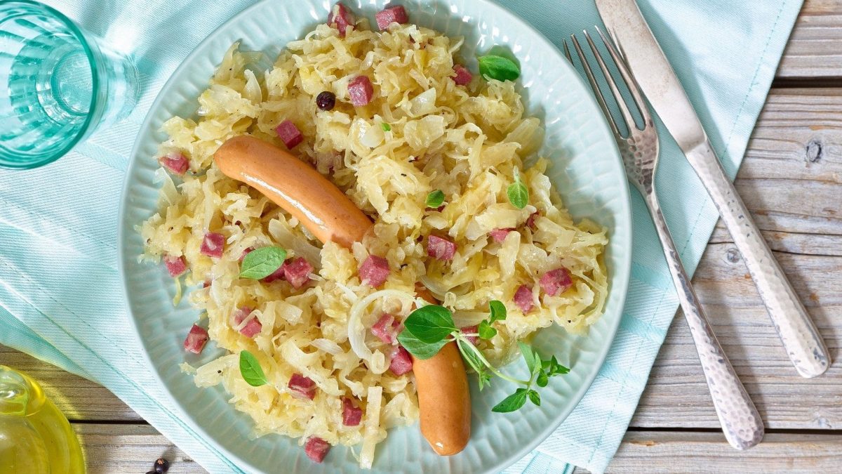 Der hellblaue Teller ist randvoll gefüllt mit Sauerkraut mit Würstchen.