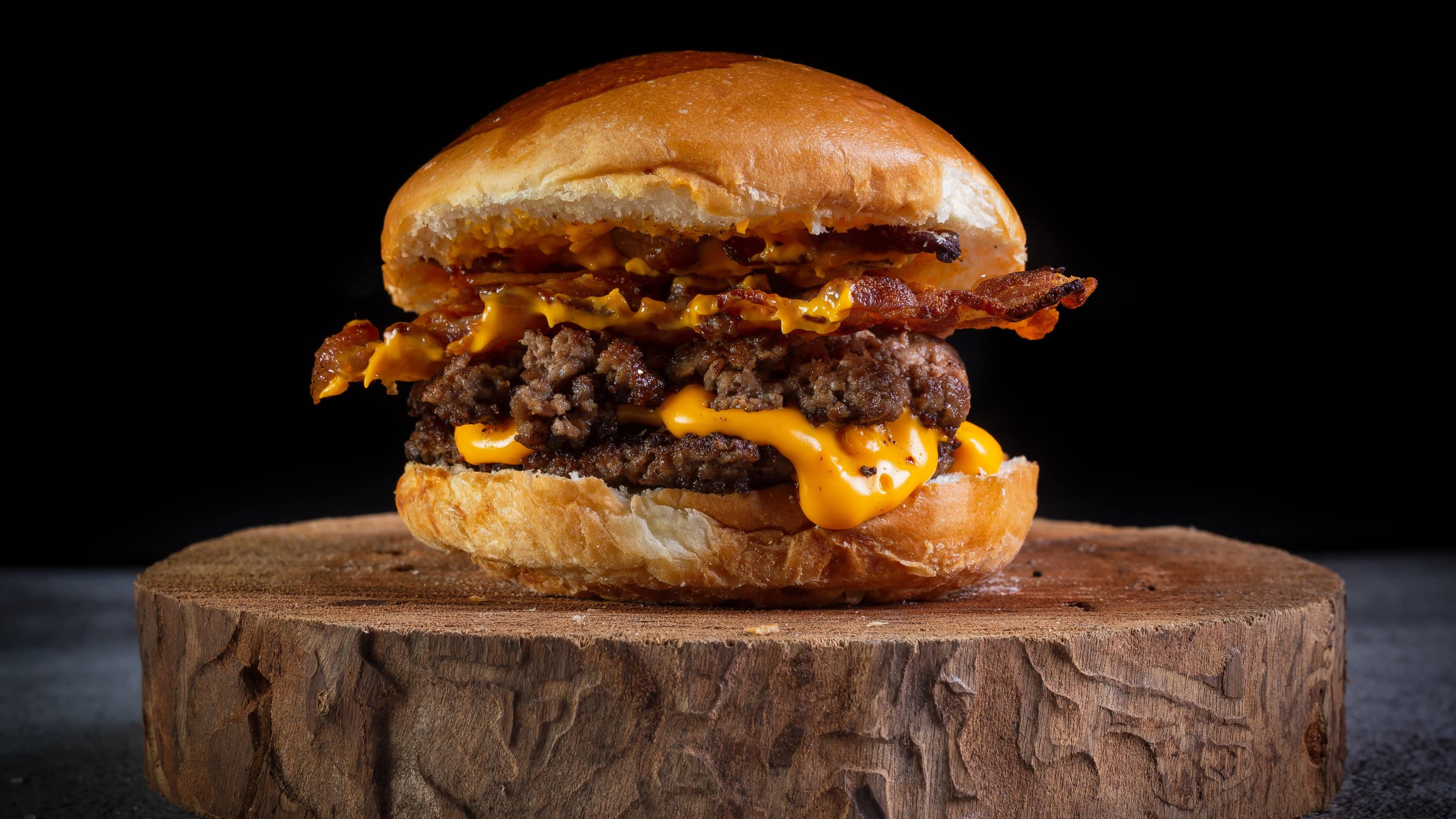 Unser Smashed Bacon-Cheeseburger liegt auf einem Holzbrett.