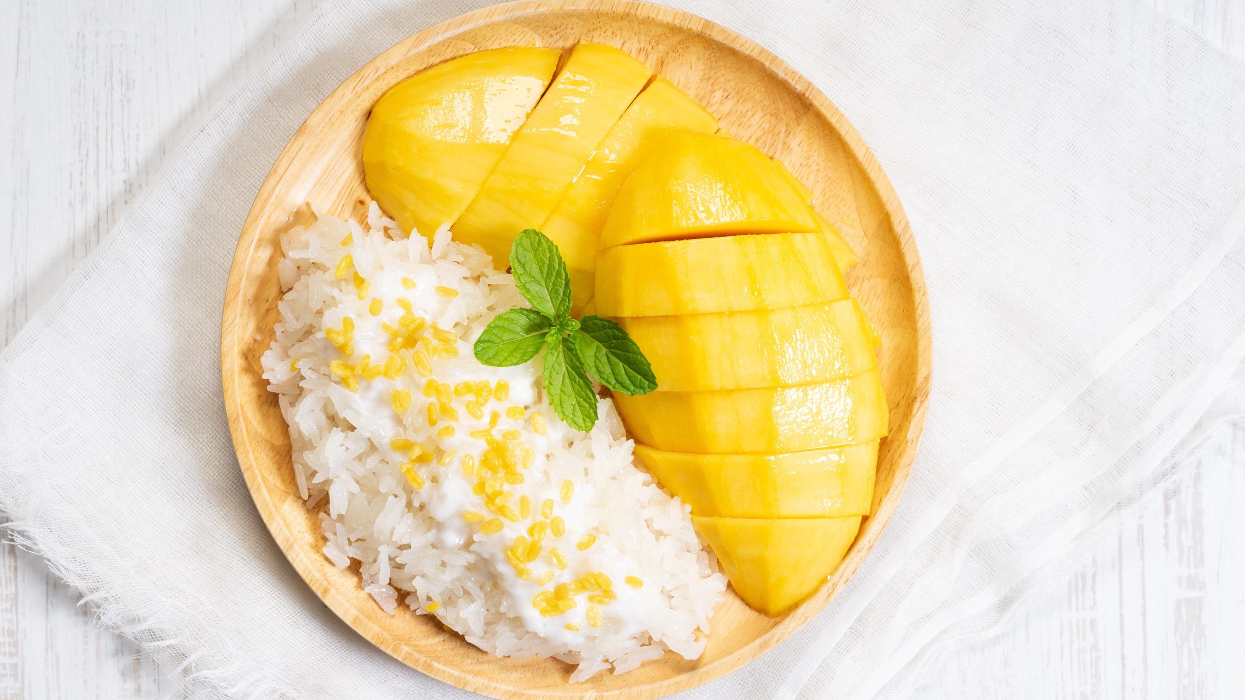 Sticky Rice mit geschnittener Mango und Kokossauce, dekoriert mit einem Minzblatt.