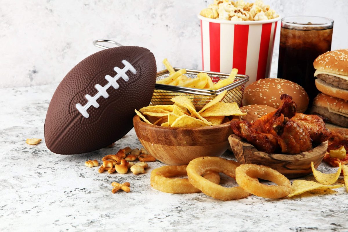 veganes Fingerfood wie Zwiebelringe, Burger, Pommen und Chips, daneben liegt ein Football.