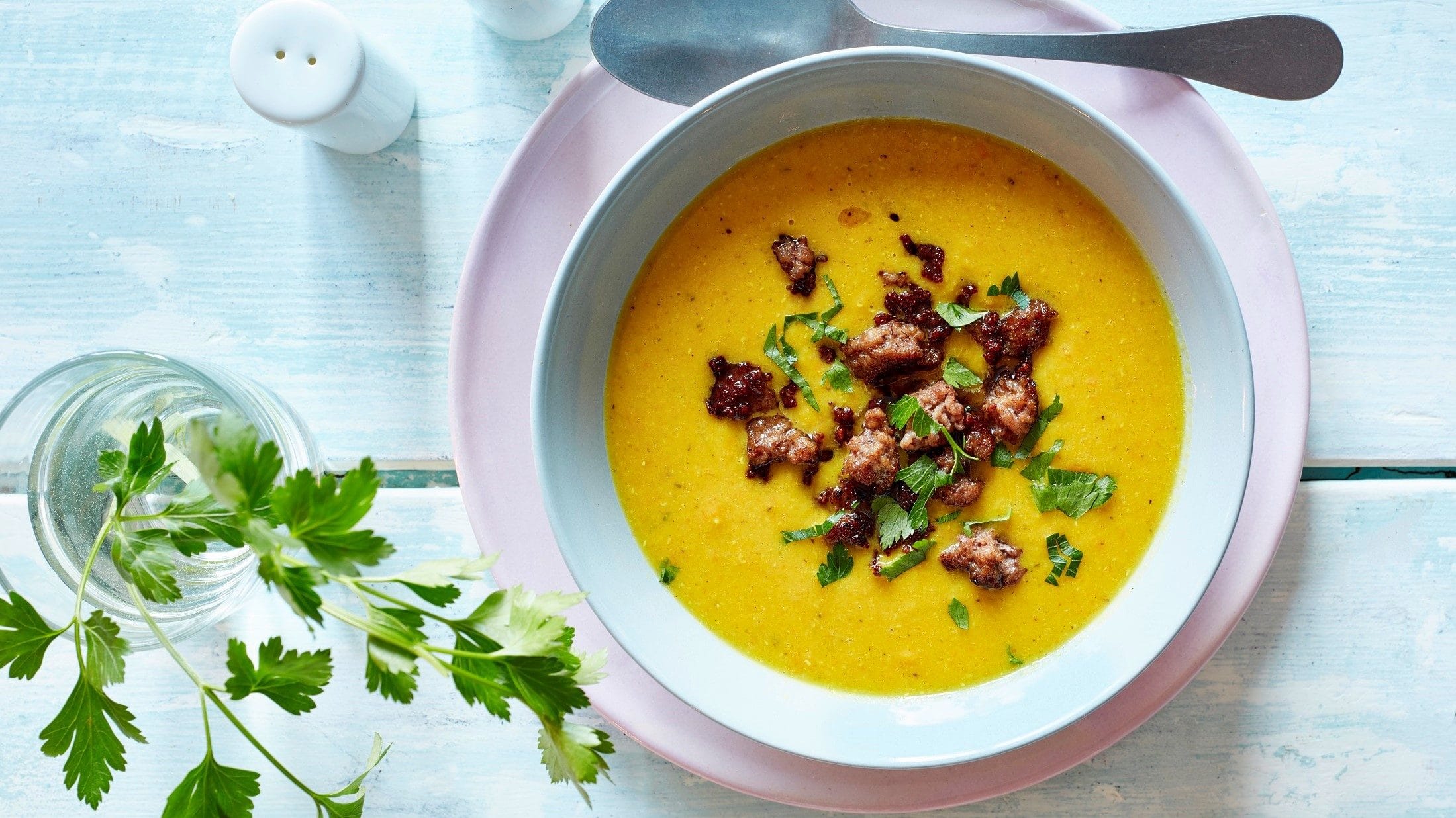 Unsere Curry-Suppe mit Hackfleisch steht angerichtet in einer Suppenschüssel und garniert mit Petersilie auf dem Tisch.