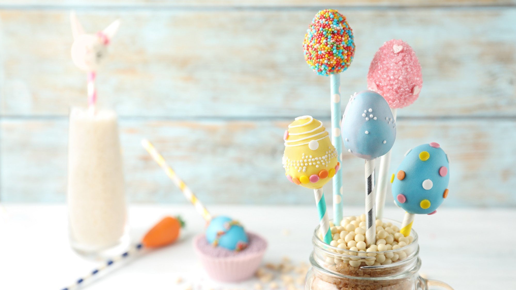 In einem Einmachglas stehen fünf Oster-Cakepops am Stiel. Sie sind in unterschiedlichen Farben dekoriert und mit Streuseln bestreut.