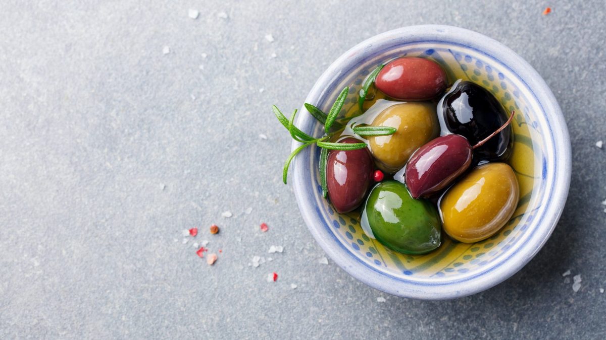 Unsere verschiedenfarbig marinierten Oliven liegen in einer Mini-Schüssel auf dem Tisch.