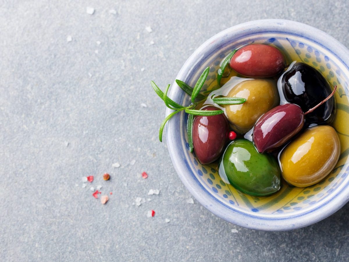 Unsere verschiedenfarbig marinierten Oliven liegen in einer Mini-Schüssel auf dem Tisch.