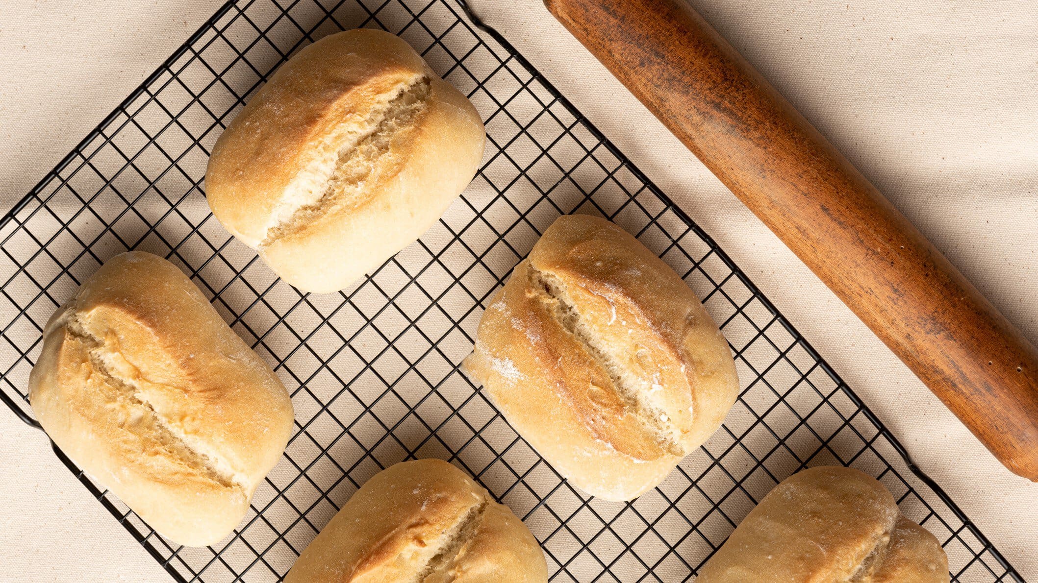 Auf einem Ofengitter liegen mehrere selbstgemachte Brötchen ohne Gluten. Sie sind goldbraun gebacken.