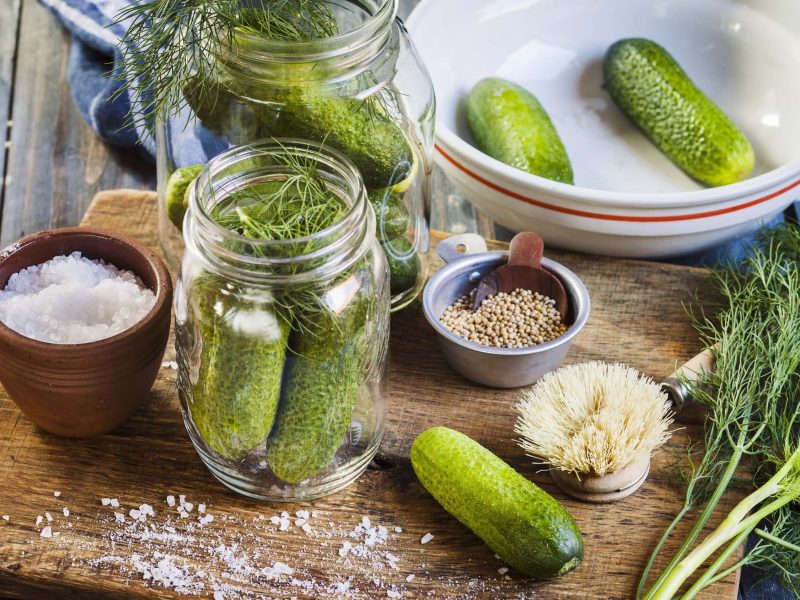 Salz-Dill-Gurken selbst machen – auf einem Brett mit Salz, frischem Dill, Senfkörnern, auf einem hölzernen Tisch
