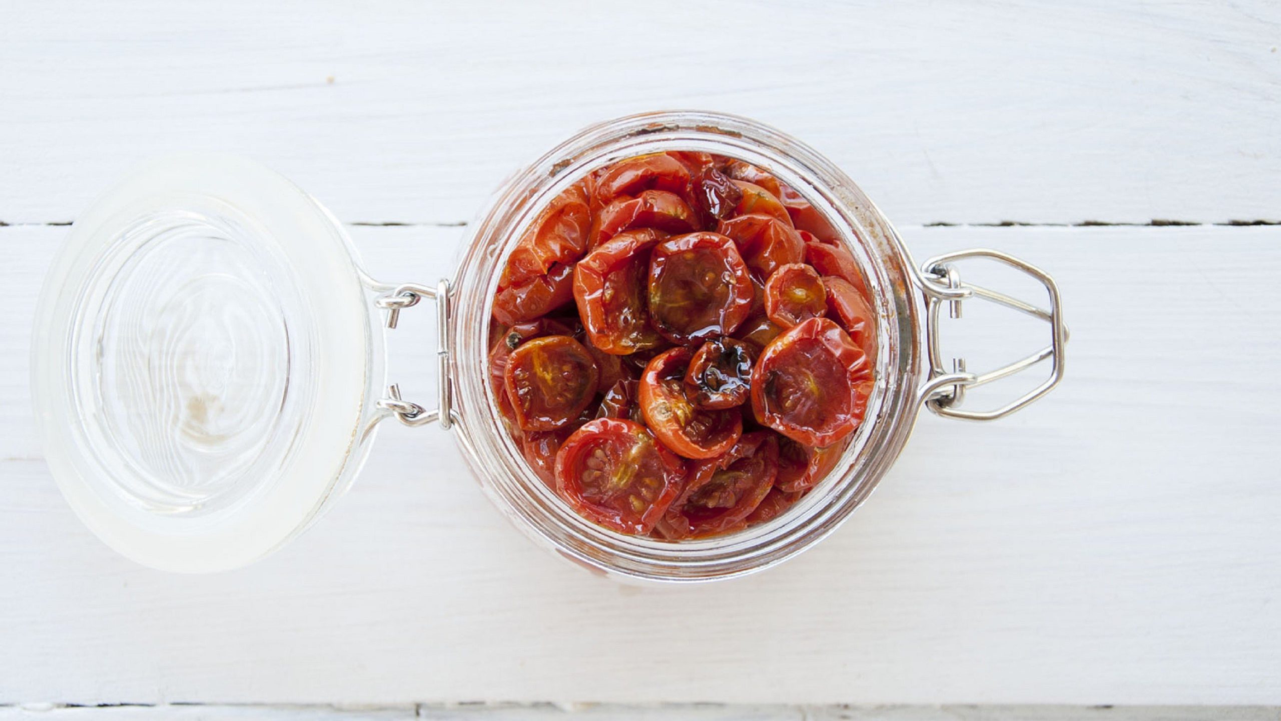 Selbst getrocknete Tomaten in einem offenen Glas aus der Vogelperspektive aufgenommen, auf einem hellen Holztisch.