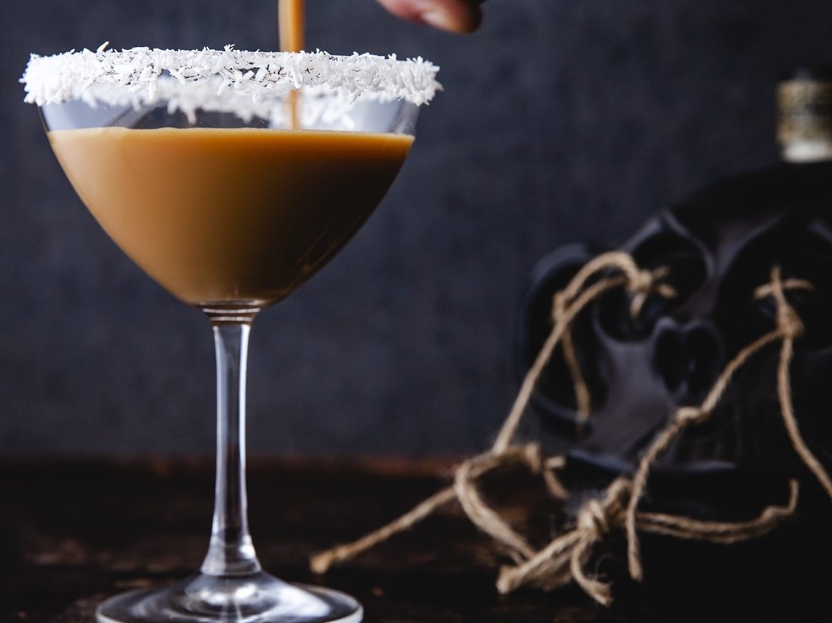 Auf einem Tisch steht ein Cocktail mit Eierlikör, Rum und Espresso. Der Rand des Glases ist mit Kokosraspeln verziert.