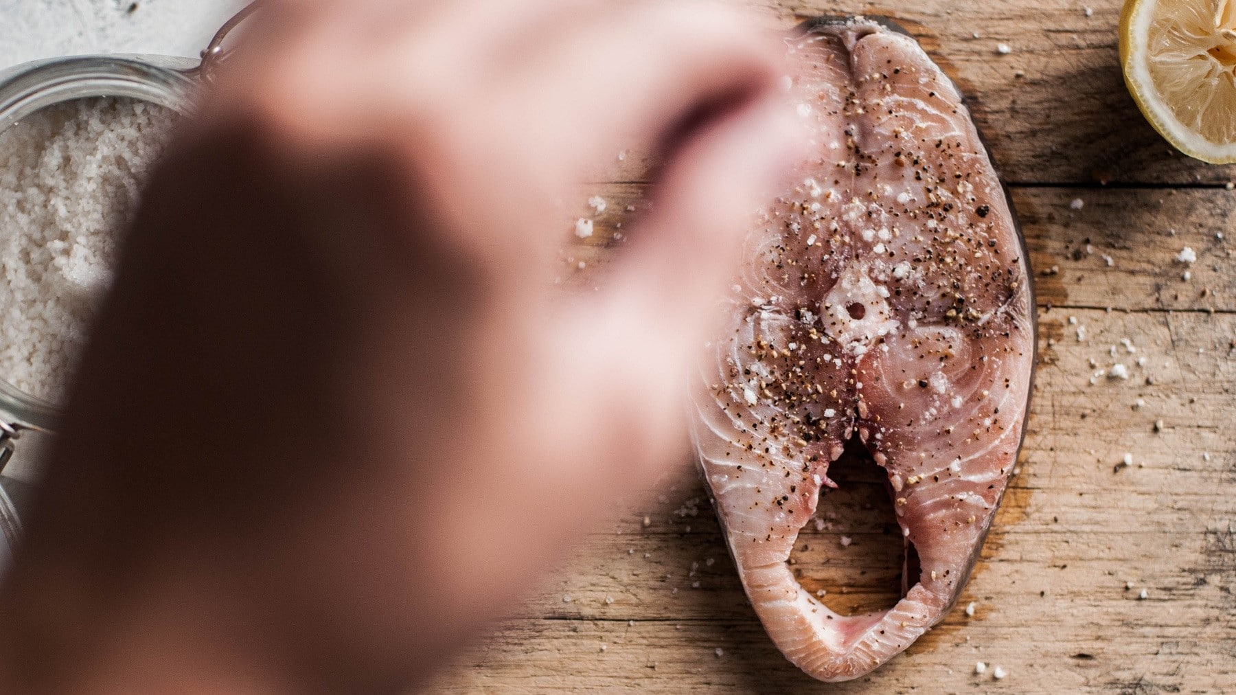 Selbst gemachtes Fisch-Gewürz wird von einer Hand auf ein Stück Makrelen-Steak gestreut.