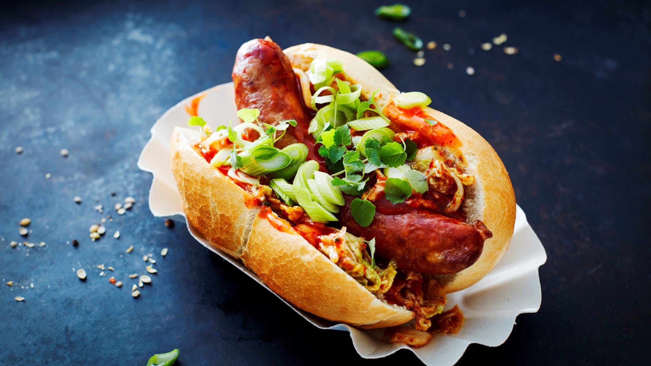 Schräge Aufnahme vom Kimchi-Hot-Dog auf einer weißen Schale und dunklem Untergrund.