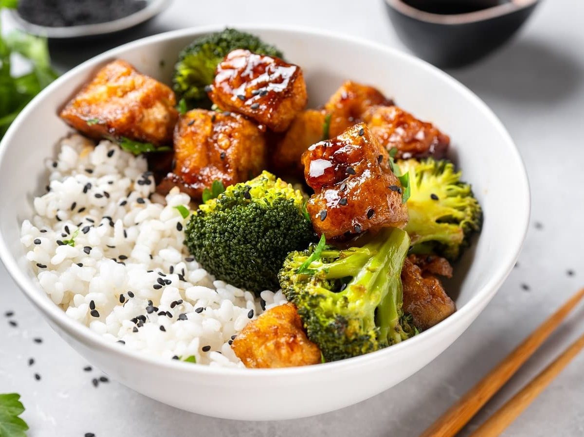 Tofu in Pfeffer-Sojasauce mit Brokkoli in einer Schüssel mit Reis neben einem Paar Stäbchen