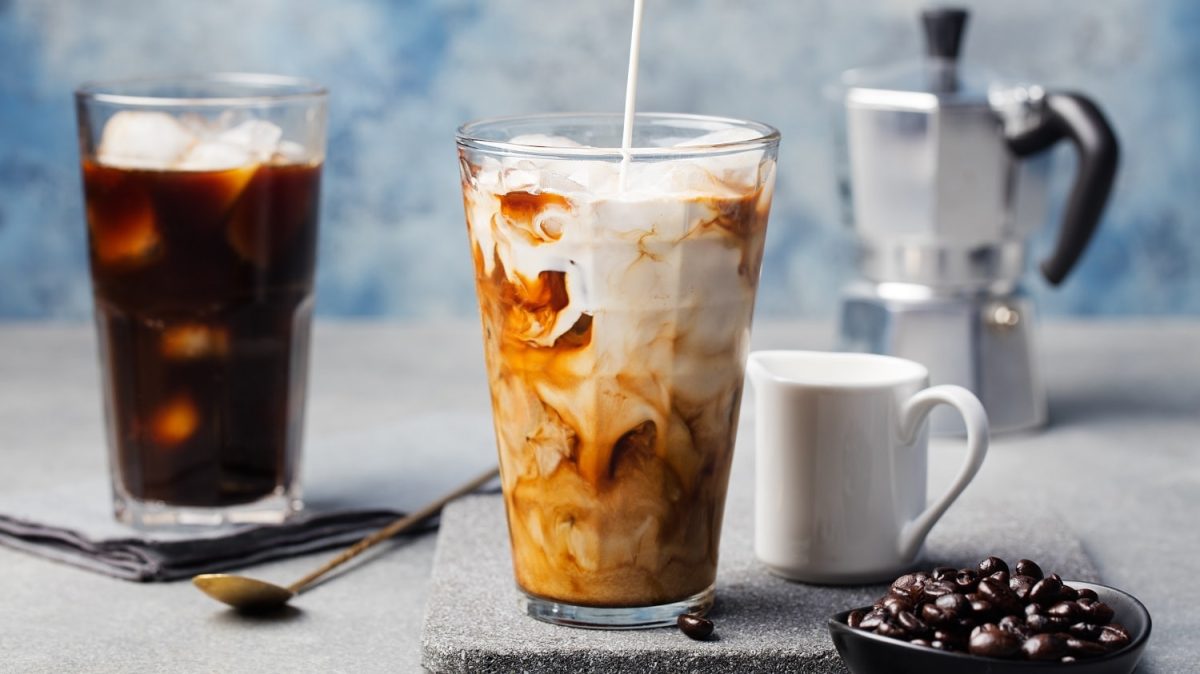 Vietnamesischer Eiskaffee in einem Glas mit Eiswürfeln und Kaffeebohnen auf einem hellgrauen Tisch