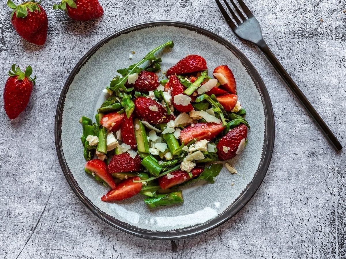 Spargelsalat mit Erdbeeren, Feta, Parmesan und Walnüssen auf hellem Teller.